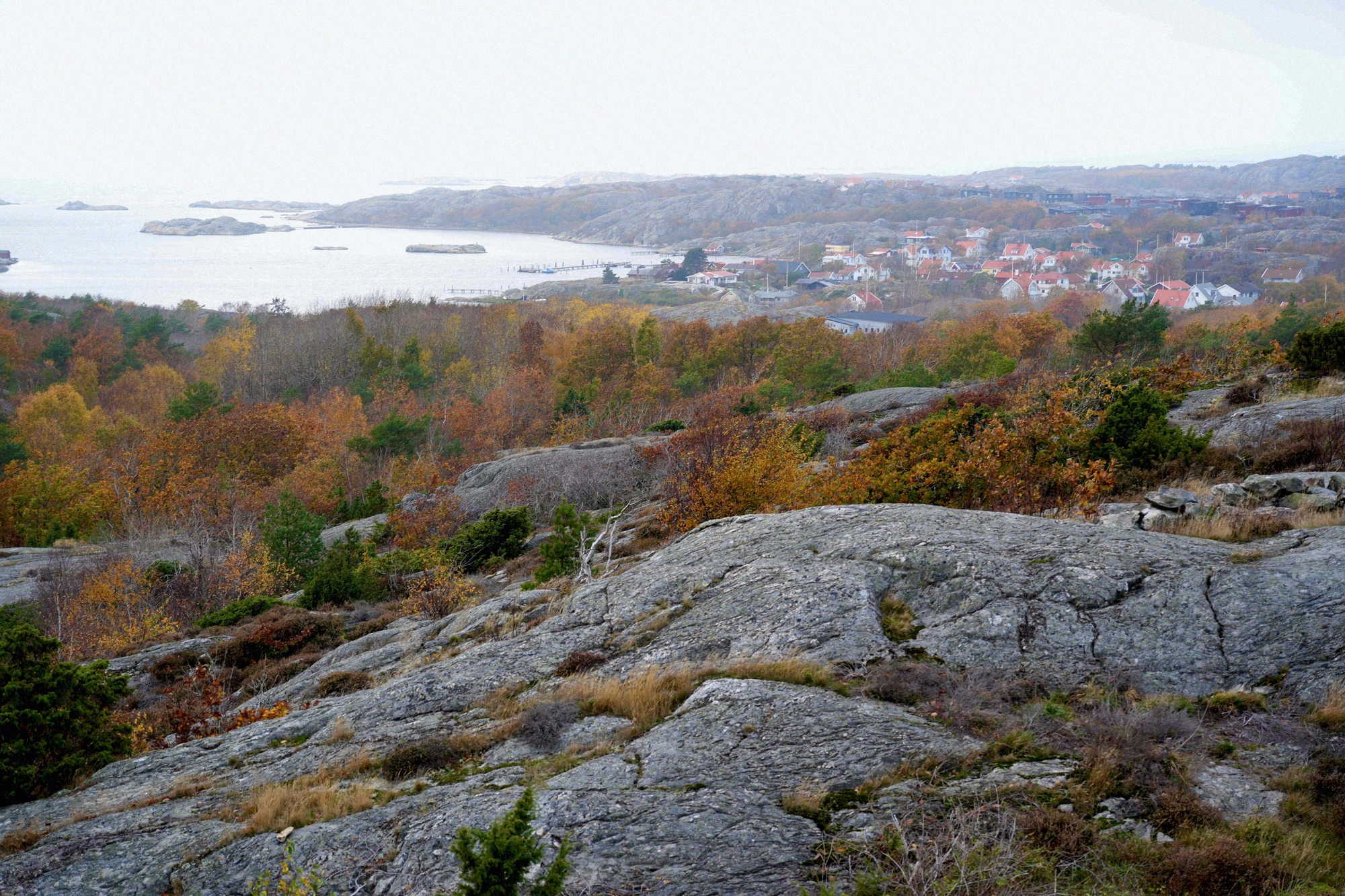 Herbstlicher Blick vom Granitfelsen über den schwedischen Schärengarten mit einem kleinen Küstendorf im Hintergrund.